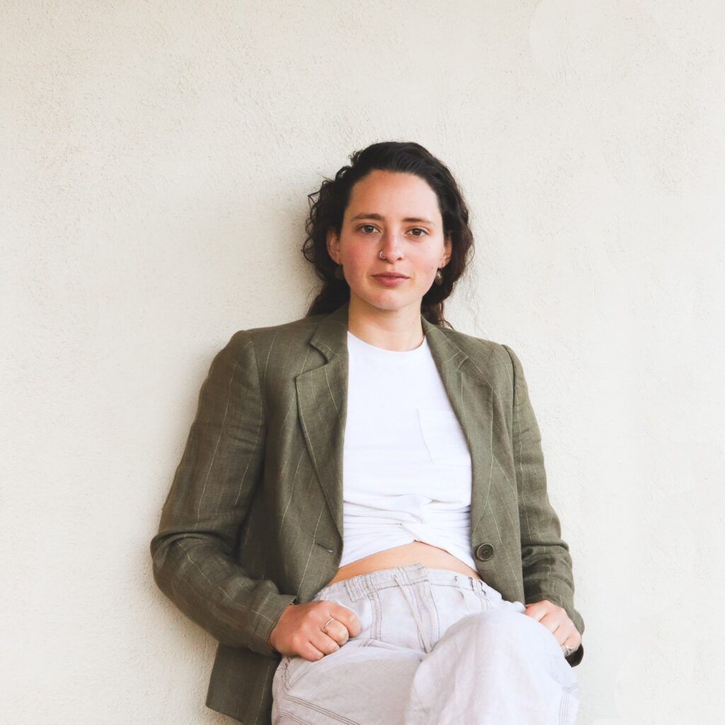 image of a smiling women with brown hair and brown eye, in white shirt and green blazer, with white background